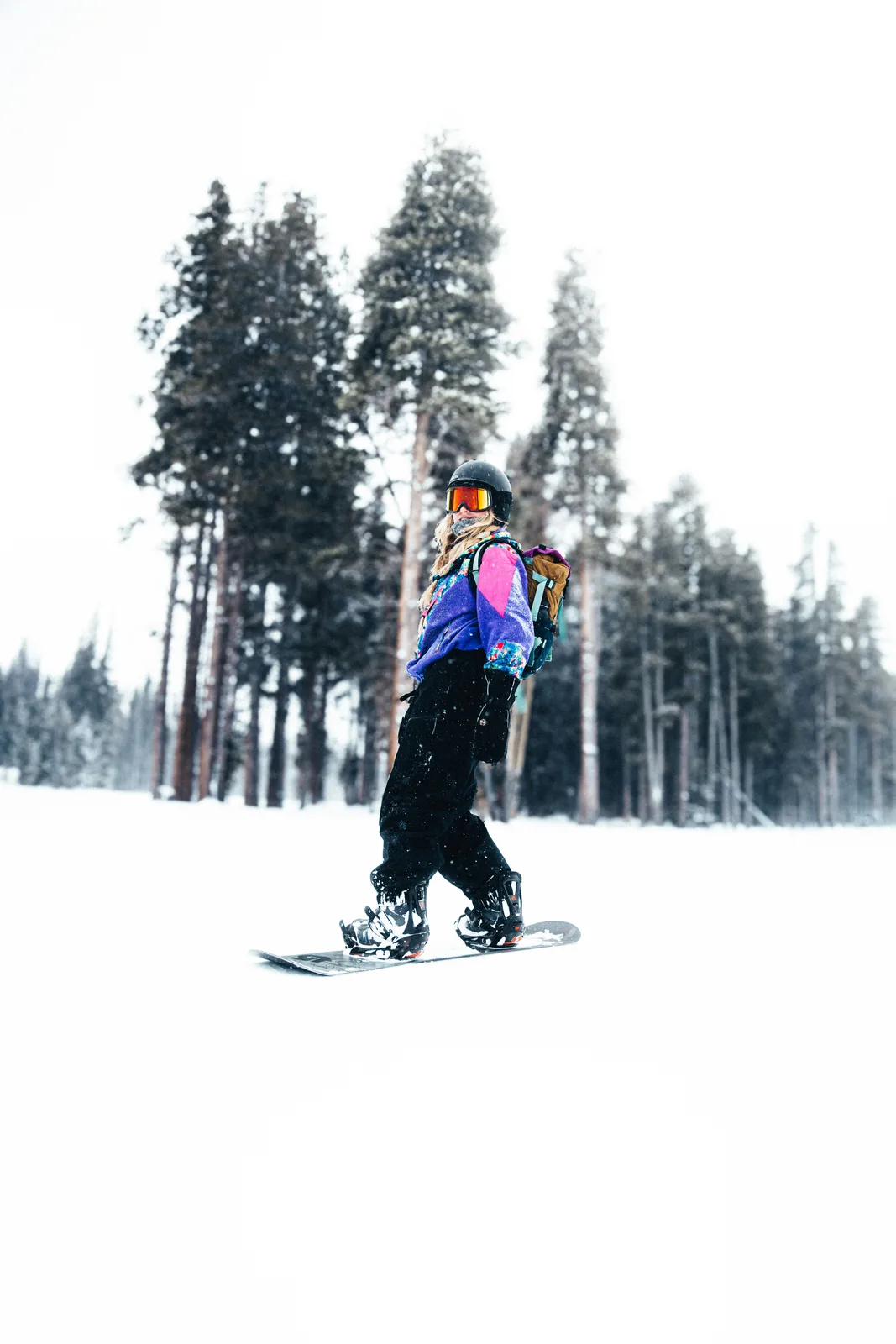 Female snowboarder standing on a snowy trail among pine trees
